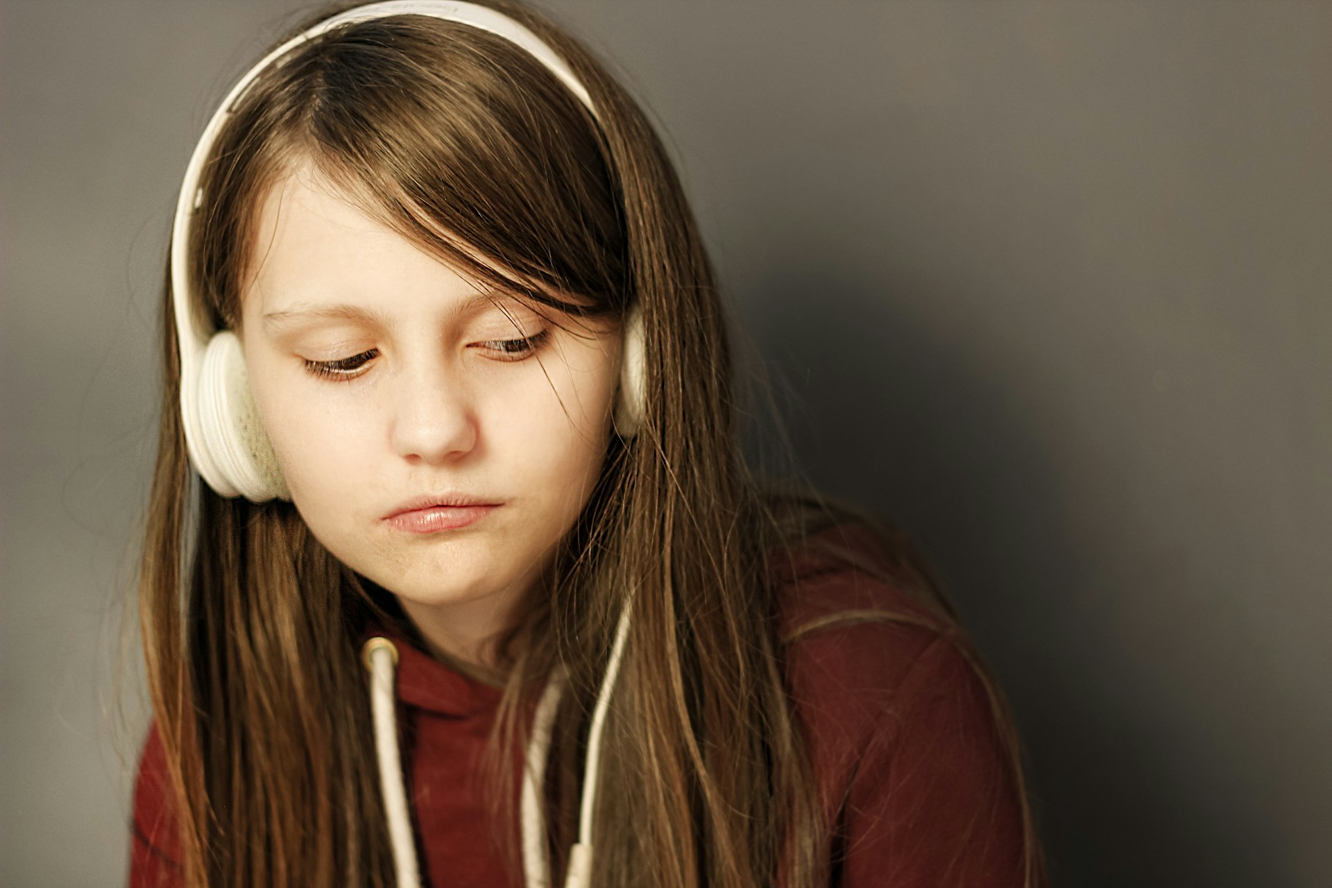 A teenage girl wearing a headphone wearing a long sleeved sweater looking sad